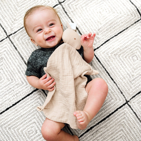 Lächelndes Baby hält das beige Schmusetuch Hase von Mikito